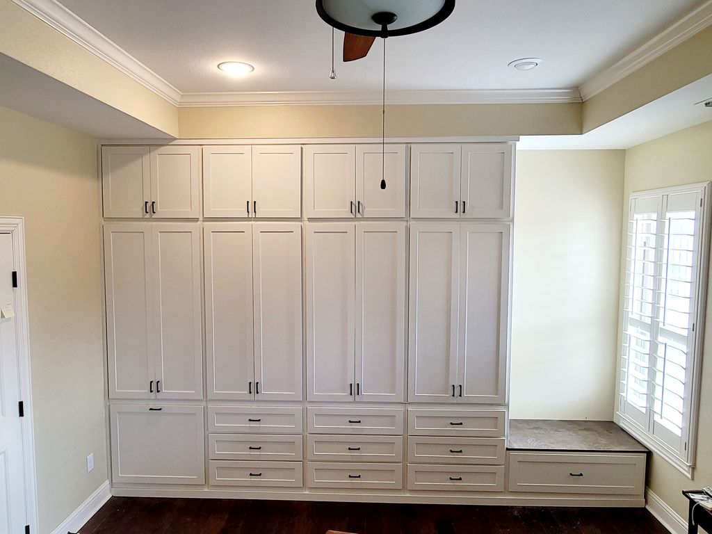 Floor-to-ceiling custom closet wall with Shaker doors, drawers and a window seat